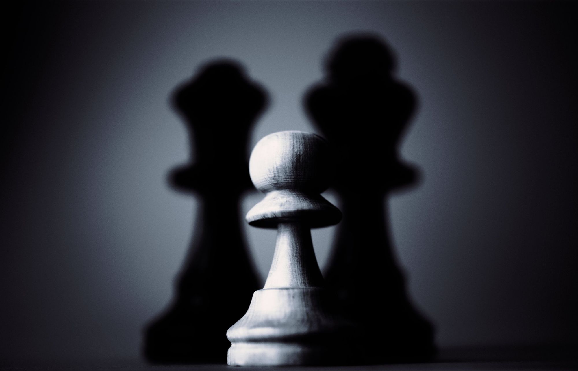A small pawn standing in front of two larger chess pieces